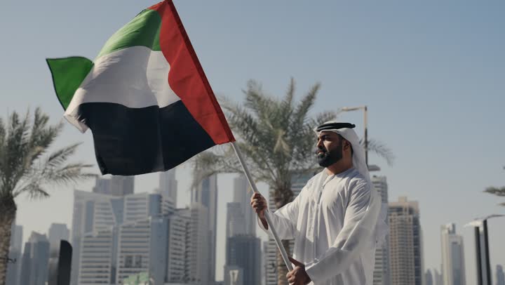 الاحتفال باليوم الوطني 2 ديسمبر، ايماءات الفخر والسعاده ، ذكرى تأسيس الاتحاد1971، التعرف على ثقافات وتاريخ شعب الامارات، إحياء حب الوطن والانتماء إليه, تصوير لرجل يرتدي الكندوره والغتره يرفع علم دولة الامارات العربية المتحدة ،  يوم استقلال الإمارات