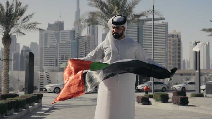 يوم استقلال الإمارات ، التعرف على ثقافات وتاريخ شعب الامارات، حب الوطن والانتماء إليه, اليوم الوطني 2 ديسمبر، تصوير لرجل يرتدي الكندوره والغتره يضع علم دولة الامارات العربية المتحدة على كتفه