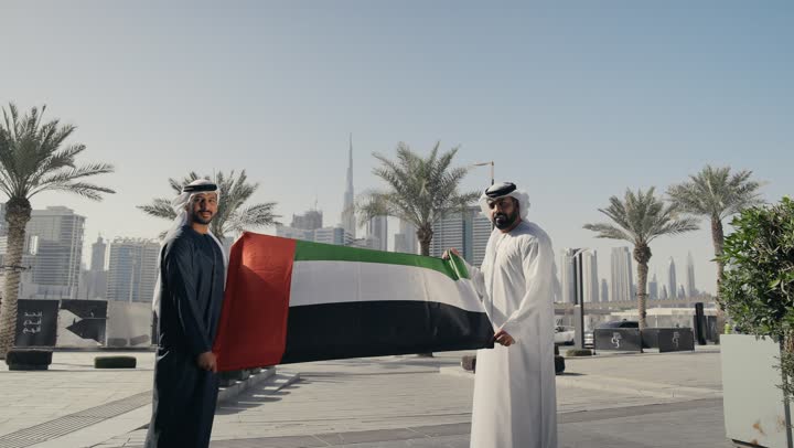 حب الوطن والانتماء إليه, الاحتفال باليوم الوطني 2 ديسمبر، يوم استقلال الإمارات ، التعرف على ثقافات وتاريخ شعب الامارات، تصوير لرجلان يرتديان الكندوره والغتره يمسكان علم دولة الامارات العربية المتحدة