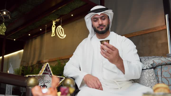 الدردشه عبر الانترنت ، تكنولوجيا وتقنيات حديثه ، جلسة الليلة الخارجية في احدى شاليهات الامارات ، دمج التكنولوجيا فى الحياه اليوميه،ضيافة شهر رمضان المبارك،شاب عربي خليجي اماراتي يرتدي الكندورة والغترة يستخدم الجوال يجلس في الهواء الطلق