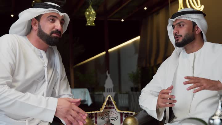 حسن الاستقبال والكرم في شهر رمضان المبارك، عادات وتقاليد شرب القهوة التقليدية، استنشاق الهواء النقي ، الاستمتاع بالاجواء الرمضانيه السعيده ، قضاء اوقات ممتعه مع الاصدقاء الجلسة الليلة الخارجية في احدى شاليهات الامارات، صديقان عربيان خليجيان اماراتيان يرتديان الكندورة والغترة يجلسان في الهواء الطلق