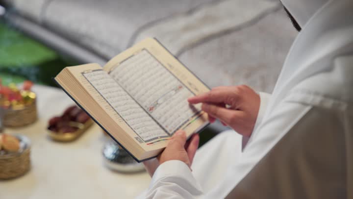 الجلوس فى احدي الشاليهات الاماراتيه ، الإكثار من ذكر الله تعالى، تلاوة وقراءة القرآن الكريم وتدبر معانيه، الاجتهاد في العبادة، الشعور بالخشوع والطمأنينة، شاب عربي خليجي اماراتي يرتدي الكندوره والغتره يحمل بيده المصحف الشريف، التقرب الى الله في شهر رمضان