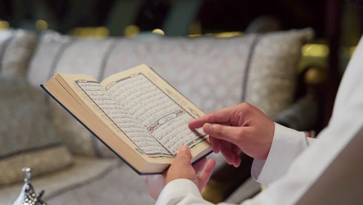 الجلوس فى احدي الشاليهات الاماراتيه ، الإكثار من ذكر الله تعالى، تلاوة وقراءة القرآن الكريم وتدبر معانيه، الشعور بالخشوع والطمأنينة، الاجتهاد في العبادة، شاب عربي خليجي اماراتي يرتدي الكندوره والغتره يحمل بيده المصحف الشريف، التقرب الى الله في شهر رمضان
