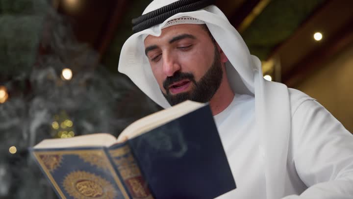 تلاوة وقراءة القرآن الكريم وتدبر معانيه، الشعور بالخشوع والطمأنينة، الجلوس فى احدي الشاليهات الاماراتيه ، الإكثار من ذكر الله تعالى، الاجتهاد في العبادة، شاب عربي خليجي اماراتي يرتدي الكندوره والغتره يحمل بيده المصحف الشريف، التقرب الى الله في شهر رمضان
