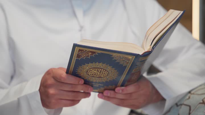 اسلاميات وعباده ، الإكثار من ذكر الله تعالى، التقرب الى الله في شهر رمضان، الجلوس فى احدي الشاليهات الاماراتيه ، تلاوة وقراءة القرآن الكريم وتدبر معانيه، الشعور بالخشوع والطمأنينة، الاجتهاد في العبادة، شاب عربي خليجي اماراتي يرتدي الكندوره والغتره يحمل بيده المصحف الشريف