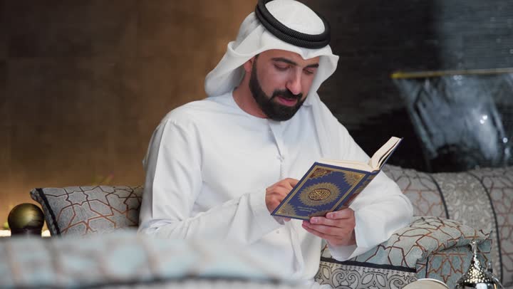 التقرب الى الله في شهر رمضان، الجلوس فى احدي الشاليهات الاماراتيه ، الإكثار من ذكر الله تعالى، تلاوة وقراءة القرآن الكريم وتدبر معانيه، الشعور بالخشوع والطمأنينة، الاجتهاد في العبادة، شاب عربي خليجي اماراتي يرتدي الكندوره والغتره يحمل بيده المصحف الشريف