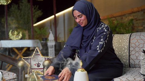 تلاوة وتحفيظ القرآن الكريم ، جلسات خارجية في الهواء الطلق ، الجلوس فى احدي الشاليهات الاماراتيه ، أدعية وأذكار، زينة شهر رمضان، المناسبات الدينية والأعياد الإسلامية، قراءة القرآن الكريم، امراه عربية خليجية اماراتيه ترتدي العباءه والحجاب تمسك بيدها كتاب الله تعالي ، إستقبال شهر رمضان، أجواء رمضانية