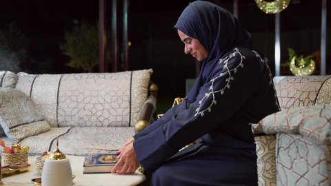 جلسات خارجية في الهواء الطلق ، الجلوس فى احدي الشاليهات الاماراتيه ، أدعية وأذكار، تلاوة وتحفيظ القرآن الكريم ، زينة شهر رمضان، المناسبات الدينية والأعياد الإسلامية، قراءة القرآن الكريم، امراه عربية خليجية اماراتيه ترتدي العباءه والحجاب تمسك بيدها كتاب الله تعالي ، إستقبال شهر رمضان، أجواء رمضانية