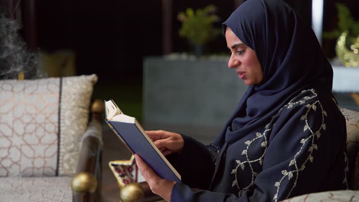 إستقبال شهر رمضان، المناسبات الدينية والأعياد الإسلامية، امراه عربية خليجية اماراتيه ترتدي العباءه والحجاب تمسك بيدها القران الكريم ، أجواء رمضانية ،كتاب الله تعالى ، تلاوة وتحفيظ القرآن الكريم ، جلسات خارجية في الهواء الطلق ، أدعية وأذكار، زينة شهر رمضان، قراءة القرآن الكريم