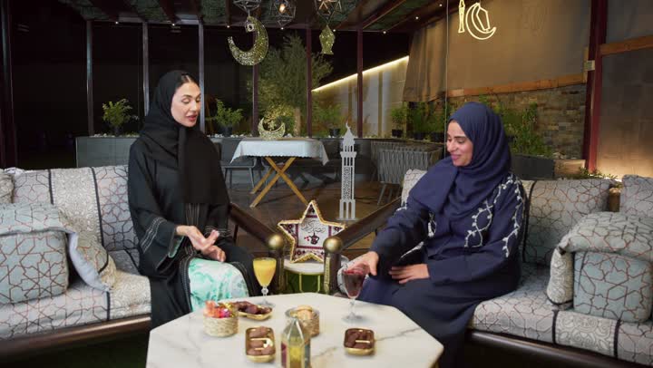 ايماءات السرور والسعاده ، حسن الاستقبال وكرم الضيافة في شهر رمضان، جلسة ليلية خارجية في إحدى شاليهات الامارات، قضاء وقت ممتع مع الأصدقاء ، الاستمتاع بشرب المشروبات البارده ،صديقتان عربيتان خليجيتان اماراتيان ترتديان العباءة والحجاب تجلسان في الهواء الطلق يتبادلان الاحاديث والاخبار