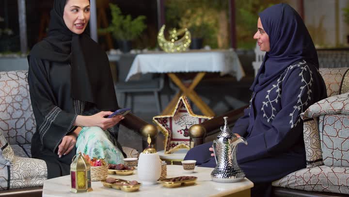 زينه وديكورات رمضانيه ، صديقتان عربيتان خليجيتان اماراتيان ترتديان العباءة والحجاب تجلسان في الهواء الطلق يتبادلان الاحاديث والاخبار بتعابير السرور، جلسة ليلية خارجية في إحدى شاليهات الامارات، حسن الاستقبال وكرم الضيافة في شهر رمضان، قضاء وقت ممتع مع الأصدقاء