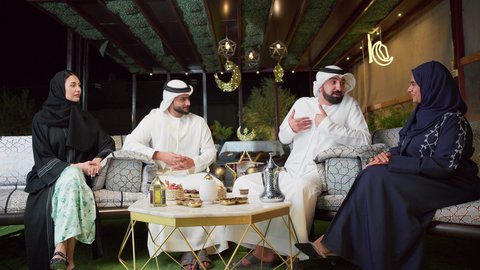 الحوار والنقاش مع الاهل ، عائله عربيه خليجيه اماراتيه تجلس في شاليه سياحي يقومون بتبادل الاحاديث بتعابير السرور، حسن الاستقبال وكرم الضيافة في شهر رمضان المبارك، الاستمتاع بتناول المشروبات الباردة ، زينة وديكور رمضاني، قضاء وقت ممتع مع العائله في الهواء الطلق
