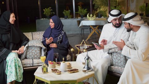 حسن الاستقبال وكرم الضيافة في شهر رمضان المبارك، الاستمتاع بتناول المشروبات الباردة ، زينة وديكور رمضاني، قضاء وقت ممتع مع العائله في الهواء الطلق، عائله عربيه خليجيه اماراتيه تجلس في شاليه سياحي يقومون بتبادل الاحاديث بتعابير السرور