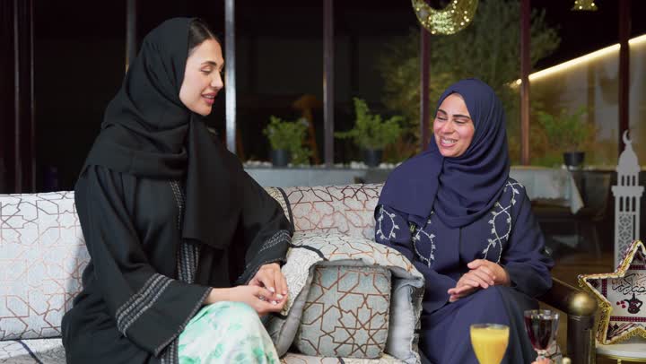 Warm welcome and hospitality in the month of Ramadan, spending a pleasant time with friends, an outdoor evening gathering in one of the chalets in the Emirates, two Arab Gulf Emirati friends wearing the abaya and hijab sitting in the open air exchanging conversations and news with expressions of pleasure