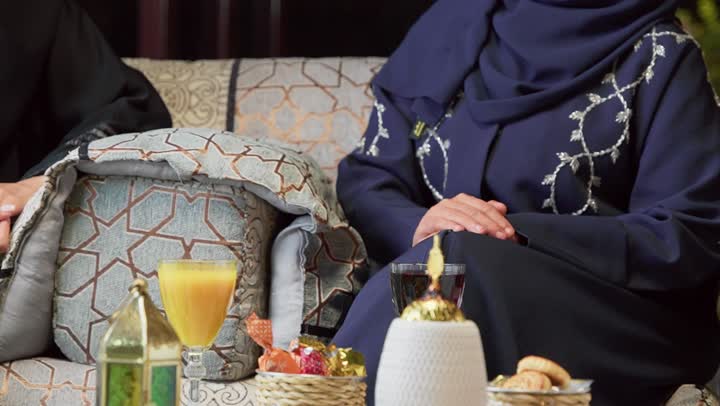 قضاء وقت ممتع مع الأصدقاء، حسن الاستقبال وكرم الضيافة في شهر رمضان، جلسة ليلية خارجية في إحدى شاليهات الامارات، صديقتان عربيتان خليجيتان اماراتيان ترتديان العباءة والحجاب تجلسان في الهواء الطلق يتبادلان الاحاديث والاخبار بتعابير السرور