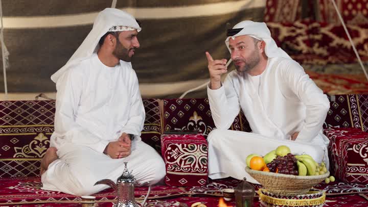 عادات وتقاليد المجلس الشعبي، رجلان عربيان خليجيان اماراتيان يجلسان امام شعله الحطب، كرم وحسن الضيافه العربيه، شاب اماراتي يشير الي شئ ما، جلسه وكشته برشبابيه