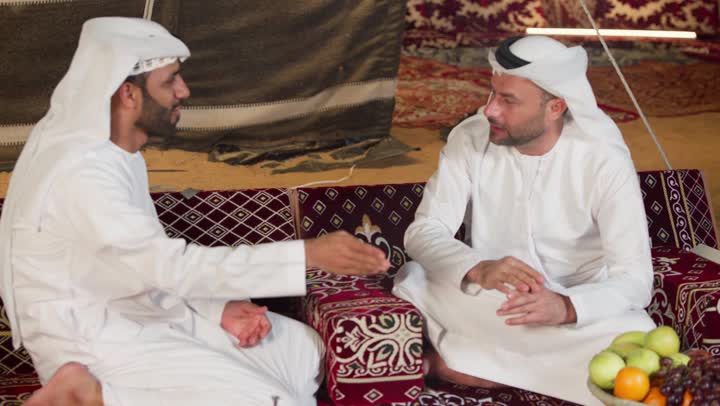 شاب عربي خليجي اماراتي يرتدي الكندوره والغتره يقوم بالتحدث مع صديقه عن السوالف اليوميه، ايماءات يدين تدل على الاشاره والتلويح، اكرام الضيف و حسن الضيافه والاستقبال، التسامر والتحدث في امر ما