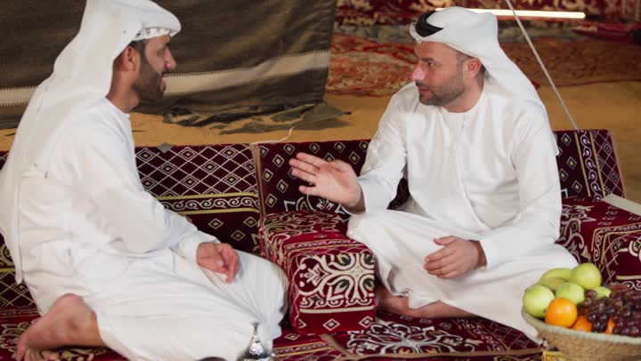 التسامر والتحدث في امر ما، ايماءات يدين تدل على الاشاره والتلويح، شاب عربي خليجي اماراتي يرتدي الكندوره والغتره يقوم بالتحدث مع صديقه عن السوالف اليوميه، اكرام الضيف و حسن الضيافه والاستقبال