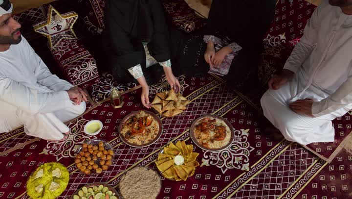 تقديم اشهي المأكولات والمقبلات للاصدقاء، تبادل المأكولات والمقبلات بين الاصدقاء، التجمع حول مائده الافطار في شهر رمضان، اصدقاء اماراتيون يجلسون في خيمه بدويه شعبيه يقومون بتقديم المقبلات والحلوي، المجلس الشعبي التقليدي، التخيم الليلي في الصحراء