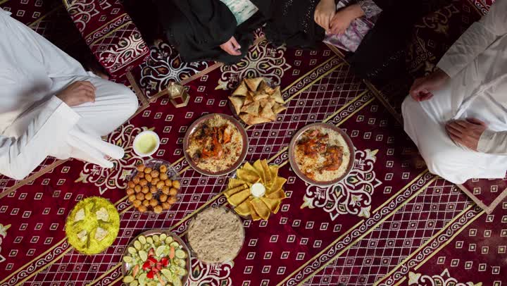 التجمع حول مائده الافطار في شهر رمضان، تصوير من الاعلي لاصدقاء اماراتيون يجلسون في خيمه بدويه شعبيه يقومون بتبادل الطعام، المجلس الشعبي التقليدي الاماراتي، مأكولات واصناف متنوعه من الارزوالمقبلات، التخيم الليلي في الصحراء