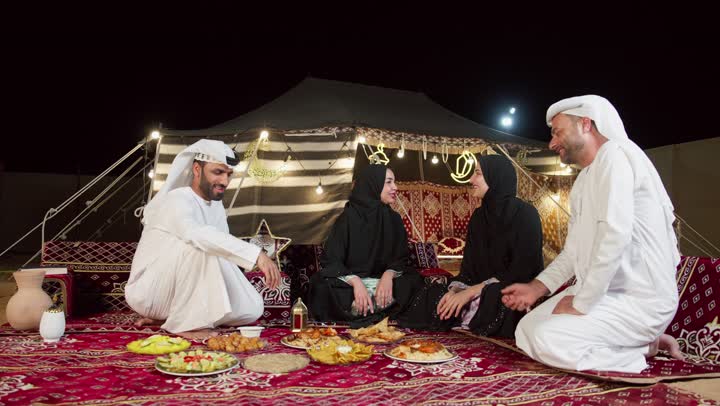 التجمع حول مائده الافطار في شهر رمضان، اصدقاء اماراتيون يجلسون في خيمه بدويه شعبيه، المجلس الشعبي التقليدي الاماراتي، مأكولات واصناف متنوعه من الارزوالمقبلات، التخيم الليلي في الصحراء