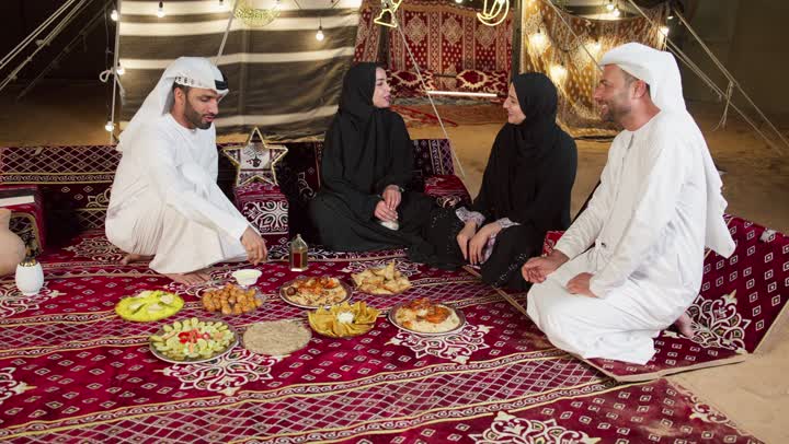 التجمع حول مائده الافطار في شهر رمضان، اصدقاء اماراتيون يجلسون في خيمه بدويه شعبيه، المجلس الشعبي التقليدي الاماراتي، مأكولات واصناف متنوعه من الارزوالمقبلات، التخيم الليلي في الصحراء