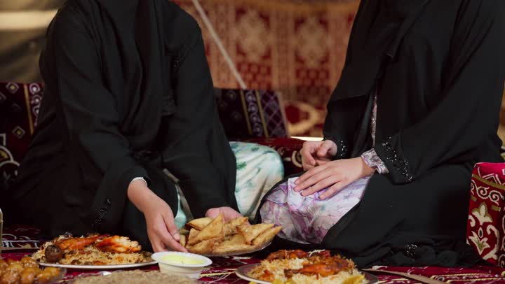 صديقتان سعوديتان ترتديان العباءه تجلسان في الخيمه ليلا، امرأه اماراتيه تقوم بتقديم المقبلات لصديقتها، مائدة طعام كبيرة مليئة بأصناف المأكولات، ديكورات شهر رمضان الكريم، التخييم في المناطق الصحراويه في الامارات