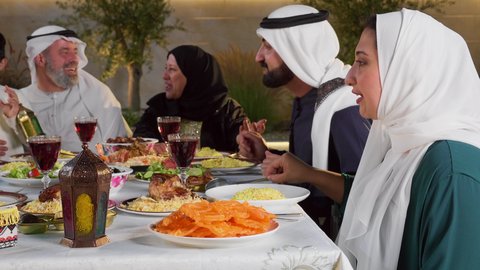 نقاش وحوار عائلي، مائده طعام مليئه بأصناف المأكولات و المقبلات الشهية، ديكور وأجواء رمضانية، تصوير مقرب لتجمع أسرة عربية خليجية اماراتية حول سفرة الإفطار في شهر رمضان المبارك، ايماءات السعادة والسرور