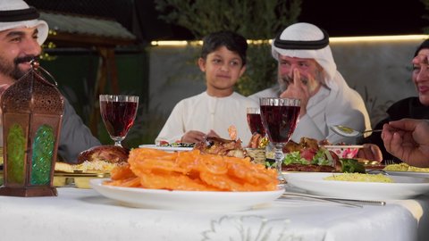 مائده طعام مليئه بأصناف المأكولات و المقبلات الشهية، ديكور وأجواء رمضانية، نقاش وحوار عائلي، تصوير مقرب لتجمع أسرة عربية خليجية اماراتية حول سفرة الإفطار في شهر رمضان المبارك، ايماءات السعادة والسرور