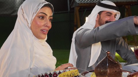 أداء فريضة الصيام، نقاش وحوار عائلي، زوجان عربيان خليجان اماراتيان يرتديان الزي التقليدي يقومان بالتجمع حول سفرة الطعام في شهر رمضان المبارك، ايماءات السعادة والسرور، حسن الضيافة و الاكرام، تصوير مقرب عربيه خليجيه  تقوم بتناول الافطار
