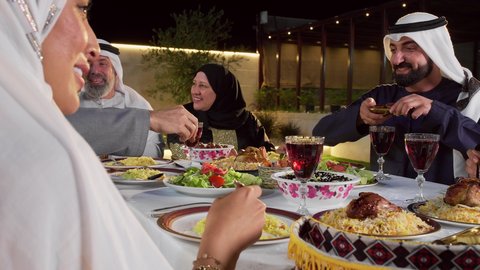مائده طعام مليئه بأصناف المأكولات و المقبلات الشهية،رجل عربي خليجي اماراتي يرتدي الزي التقليدي يقوم بتقديم طبق التمر، تجمع أسرة عربية خليجية اماراتية حول سفرة الإفطار في شهر رمضان المبارك، ايماءات السعادة والسرور، حسن الضيافة و الاكرام