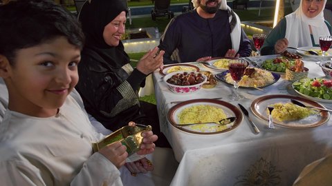 نقاش وحوار عائلي، ديكور وأجواء رمضانية، مائده طعام مليئه بأصناف المأكولات و المقبلات الشهية، تصوير مقرب لتجمع أسرة عربية خليجية اماراتية حول سفرة الإفطار في شهر رمضان المبارك، طفل خليجي يمسك الفانوس بايماءات السعاده و السرور