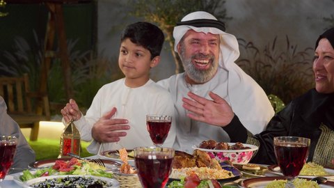 ديكور وأجواء رمضانية، نقاش وحوار عائلي، مائده طعام مليئه بأصناف المأكولات و المقبلات الشهية، تجمع أسرة عربية خليجية اماراتية حول سفرة الإفطار في شهر رمضان المبارك، طفل خليجي يمسك الفانوس بايماءات السعاده و السرور