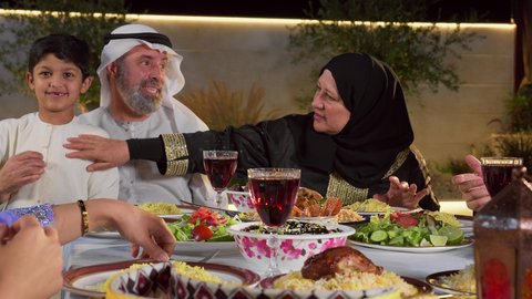 نقاش وحوار عائلي، مائده طعام مليئه بأصناف المأكولات و المقبلات الشهية، ديكور وأجواء رمضانية، تجمع أسرة عربية خليجية اماراتية حول سفرة الإفطار في شهر رمضان المبارك، ايماءات السعادة والسرور، حسن الضيافة و الاكرام
