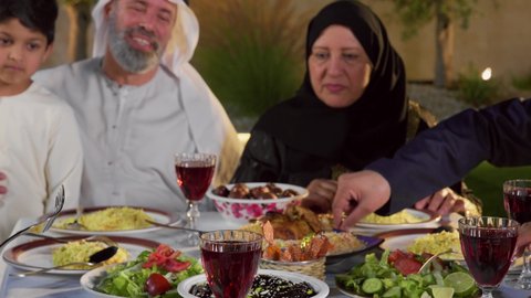 مائده طعام مليئه بأصناف المأكولات و المقبلات الشهية، ديكور وأجواء رمضانية، نقاش وحوار عائلي، تجمع أسرة عربية خليجية اماراتية حول سفرة الإفطار في شهر رمضان المبارك، ايماءات السعادة والسرور، حسن الضيافة و الاكرام
