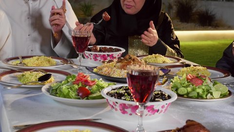 مائدة إفطار مليئة بالأصناف والمأكولات الشهية، قضاء أوقات ممتعة مع العائلة في الهواء الطلق، عائلة عربية خليجية إماراتية تقوم بتناول التمر بايماءات السعادة و السرور، الشهر الكريم والأجواء الرمضانية الروحانية