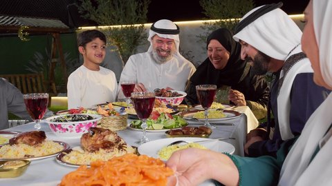 أطعمة وأكلات شعبيه تقليديه، حسن الضيافة و الاكرام، ديكور وأجواء رمضانية، تجمع أسرة عربية خليجية اماراتية حول سفرة الإفطار في شهر رمضان المبارك، ايماءات السعادة والسرور، تصويرمقرب لامراة خليجيه تقوم بتقديم طبق من الحلويات الشرقية