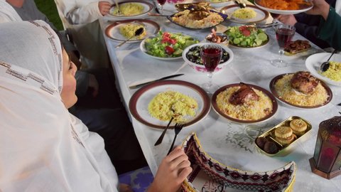 مائده طعام مليئه بأصناف المأكولات و المقبلات الشهية، نقاش وحوار عائلي، حسن الضيافة و الاكرام، ديكور وأجواء رمضانية، تجمع أسرة عربية خليجية اماراتية حول سفرة الإفطار في شهر رمضان المبارك، ايماءات السعادة والسرور، تصويرمقرب لامراة خليجيه تقوم بتقديم طبق من الحلويات الشرقية