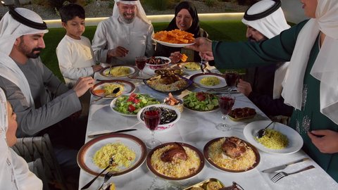 حسن الضيافة و الاكرام، مائده طعام مليئه بأصناف المأكولات و المقبلات الشهية، ديكور وأجواء رمضانية، نقاش وحوار عائلي، تجمع أسرة عربية خليجية اماراتية حول سفرة الإفطار في شهر رمضان المبارك، ايماءات السعادة والسرور، تصوير لامراة خليجيه تقوم بتقديم طبق من الحلويات الشرقية