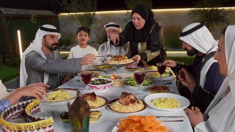 اداء فريضة الصيام، تجمع العائلة على سفرة الاكل,تصوير مقرب لامراه عربيه خليجيه اماراتية ترتدي الحجاب تقوم بتوزيع الطعام على الضيوف، الاحتفال بالاعياد و المناسبات الاسلامية, عائلة عربية خليجية اماراتية تجلس على الطاولة المليئة بالاطباق الشهية