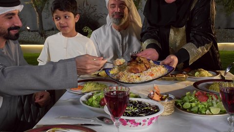 ايماءات السعادة و السرور بقدوم شهر رمضان المبارك,، تجمع العائلة على سفرة الاكل,تصوير مقرب لرجل عربي خليجي اماراتي يرتدي الزي التقليدي يقوم بغرف طبقة، الاحتفال بالاعياد و المناسبات الاسلامية, عائلة عربية خليجية اماراتية تجلس على الطاولة المليئة بالاطباق الشهية