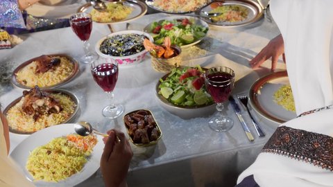 قضاء أوقات ممتعه مع العائله في الخارج، أسرة عربيه خليجيه اماراتية تقوم بتناول الطعام العائلي في أحد المطاعم، كسر الصيام عند سماع أذان المغرب، مائده إفطار مليئه بالأصناف والمأكولات الشهية، تصوير مقرب ليد رجل عربي خليجي يقوم بغرف طبق من الارز