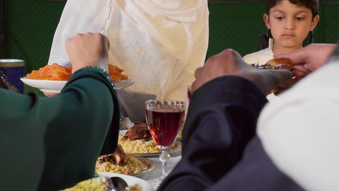 أداء فريضة الصيام، العزائم والولائم في الأعياد والمناسبات الإسلامية، أجواء دينية رمضانية، مشاركة الأطعمة و إكرام الضيف، تصوير مقرب لامراة عربيه خليجيه اماراتية ترتدي العباءه الملونه تقوم بتقديم طبق من التمر