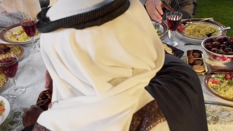 العزائم والولائم في الأعياد والمناسبات الإسلامية، أجواء دينية رمضانية، مشاركة الأطعمة و إكرام الضيف، تصوير مقرب من الخلف  لرجل عربي خليجي اماراتي يرتدي الزي التقليدي تقوم بتقديم طبق من التمر ، أداء فريضة الصيام