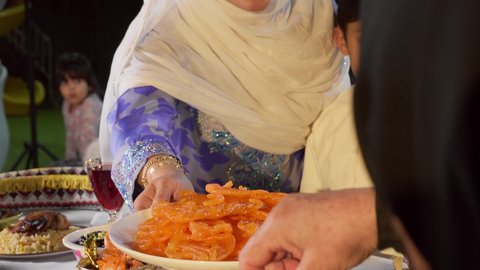 مشاركة الأطعمة و إكرام الضيف، أجواء دينية رمضانية، تصوير مقرب لامراة عربية خليجية اماراتية ترتدي الحجاب و العباءة الملونه تقوم بتقديم طبق من الحلويات الشرقية ، أداء فريضة الصيام، ايماءات السعاده و السرور