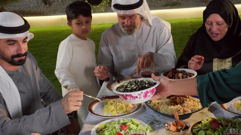 لمة الاهل على طاولة الطعام، ديكور وأجواء رمضانية، أداء فريضة الصيام ، مفهوم الترابط العائلي، أجواء وعبادات دينية إسلامية، عائله عربيه خليجيه اماراتيه تستمع بالفطارالجماعي، تصوير مقرب ليد امراة خليجيه تقوم بتقديم طبق من الورق العنب لافراد الاسره