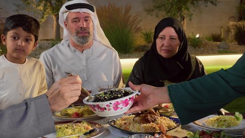 ديكور وأجواء رمضانية، أداء فريضة الصيام ، لمة الاهل على طاولة الطعام ، مفهوم الترابط العائلي، أجواء وعبادات دينية إسلامية، عائله عربيه خليجيه اماراتيه تستمع بالفطارالجماعي، تصوير مقرب ليد امراة خليجيه تقوم بتقديم طبق من الورق العنب لافراد الاسرة