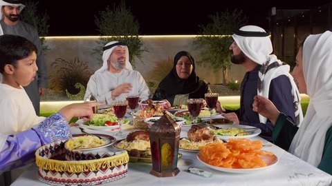 الاحتفال بالاعياد و المناسبات الاسلامية، التربية الصالحة للأبناء، سفرة إفطار مليئة بأصناف من المأكولات والمقبلات الشهية, عائلة عربية خليجية إماراتية مستمتعة بتناول الفطور في شهر رمضان, مشاركة الطعام وإكرام الوالدين، شاب اماراتي خليجي يقوم بتقبيل رأس والده
