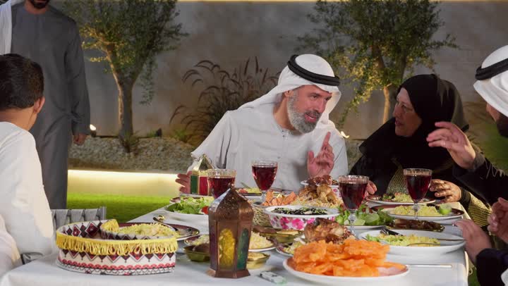 التربية الصالحة للأبناء، الاحتفال بالاعياد و المناسبات الاسلامية، سفرة إفطار مليئة بأصناف من المأكولات والمقبلات الشهية, عائلة عربية خليجية إماراتية مستمتعة بتناول الفطور في شهر رمضان, مشاركة الطعام وإكرام الوالدين، شاب اماراتي خليجي يقوم بتقبيل رأس والده
