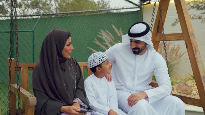 استخدام التقنيات الحديثه، زوجان عربيان خليجيان اماراتيان يجلسان برفقه ابنهم ويقومان بتوثيق اللحظات السعيده، الجلوس فى حديقه المنزل، امرأه اماراتيه برفقه عائلتها تقوم بالتقاط صور تذكاريه عبر الهاتف المحمول